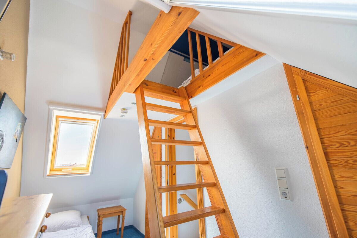 A loft bedroom with a wooden ladder, a small table, a bed, and a window.