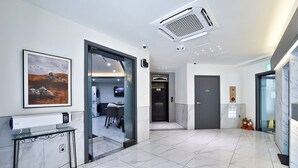 Eine moderne Hotellobby mit Marmorboden, einer Rezeption, einem gerahmten Landschaftsbild und einem Aufzug.