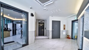 Eine moderne Hotellobby mit Glastür, Marmorboden, einem Aufzug und einem Feuerlöscher.