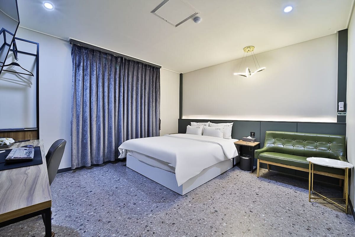 Ein modernes Hotelzimmer mit einem großen Bett, einem grünen Sofa, einem kleinen Tisch und einem Schreibtisch mit Stuhl.