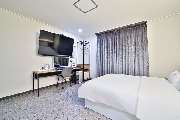 Una habitación de hotel con una cama, un escritorio con computadora, televisor y armario.