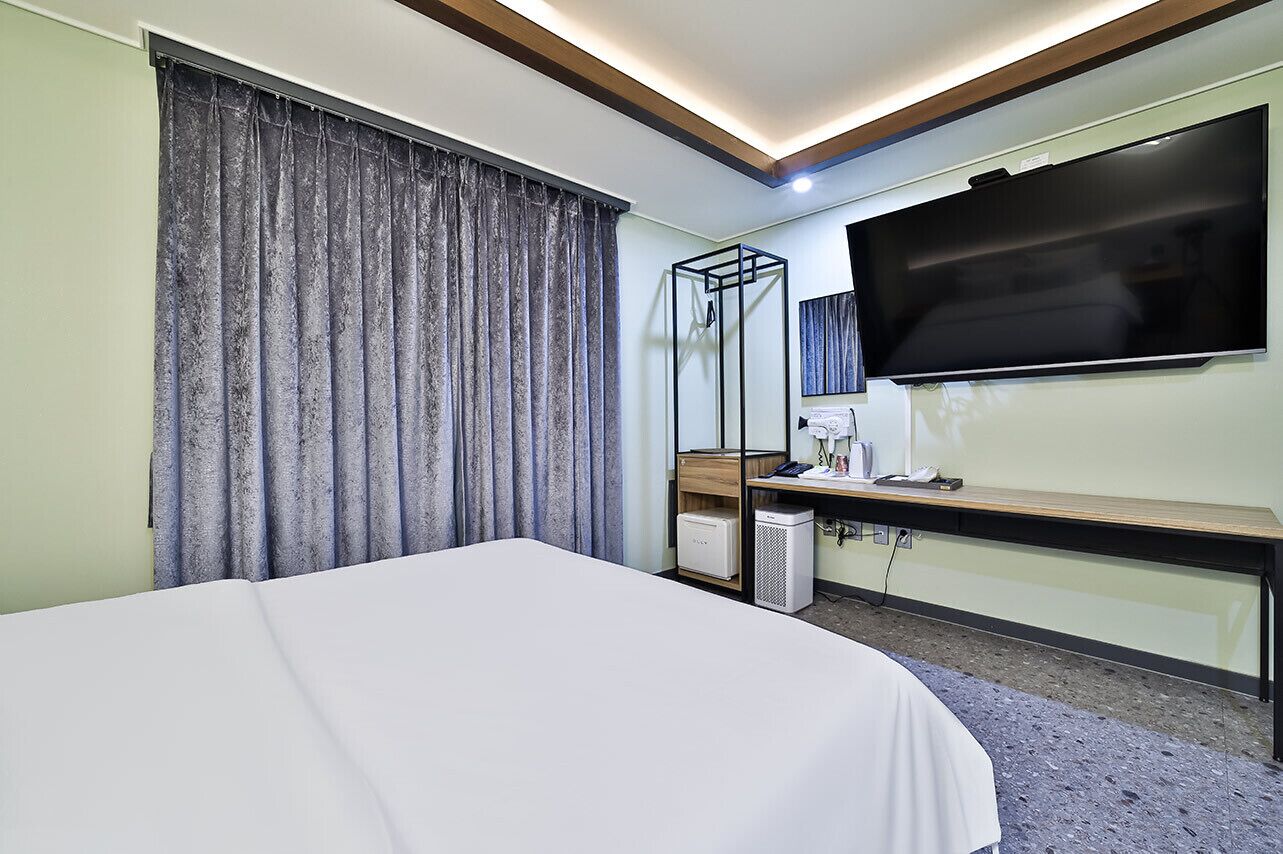 A hotel room with a large bed, a desk with a flat-screen TV, a mirror, and a heater.