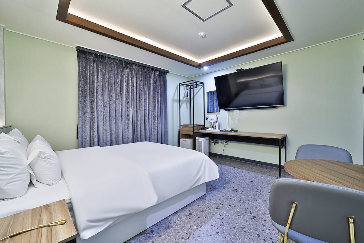 Ein Hotelzimmer mit Bett, Schreibtisch, Stuhl, Fernseher und Spiegel.