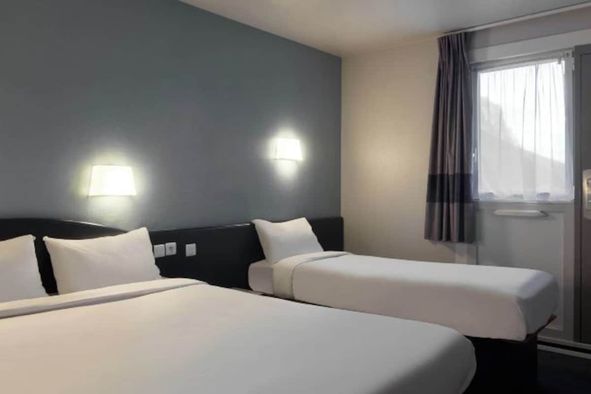Habitación de hotel con dos camas, un cabecero oscuro y dos luces fijadas a la pared.