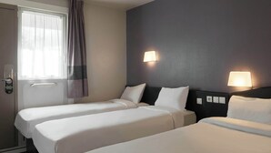 Hotellihuone, jossa on kaksi erillistä sänkyä, lukittava ovi, verhoilla varustettu ikkuna ja kaksi seinälle asennettua lamppua.