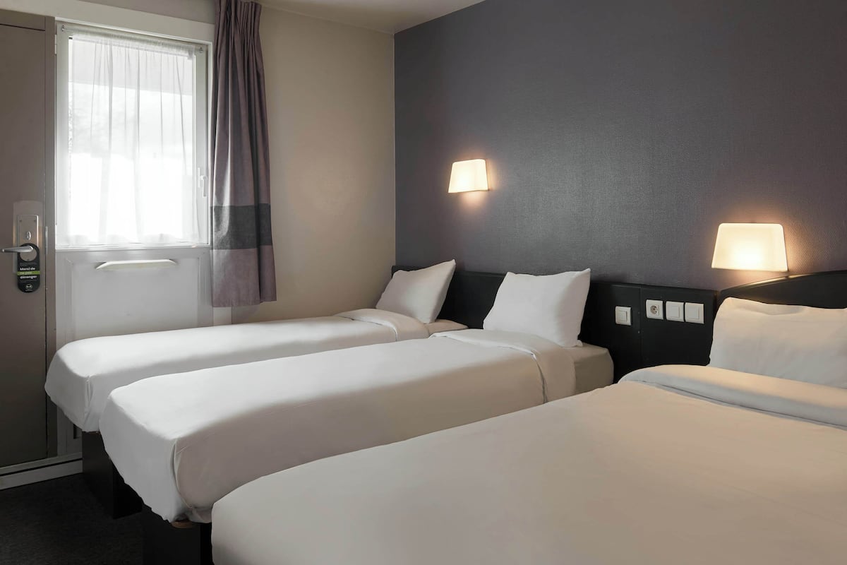 Habitación de hotel con dos camas individuales, una puerta con cerradura, una ventana con cortinas y dos lámparas fijadas a la pared.