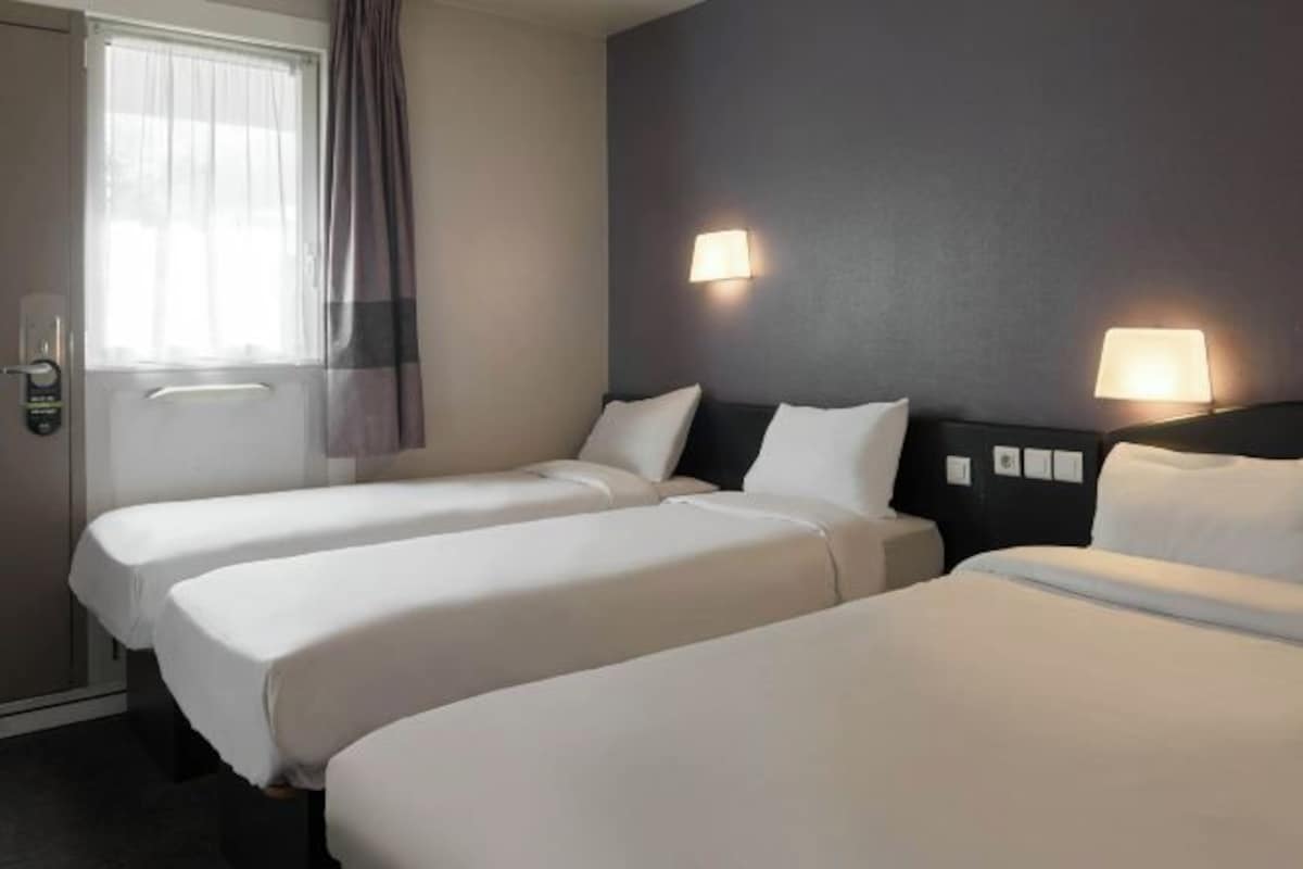 Habitación de hotel con dos camas individuales, una ventana con cortinas y lámparas fijadas a la pared.