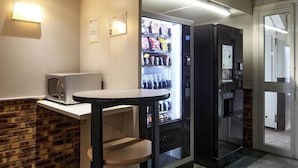 Pieni, käytännöllinen keittiönurkkaus, jossa on mikroaaltouuni, pieni pöytä ja juoma-automaatti.