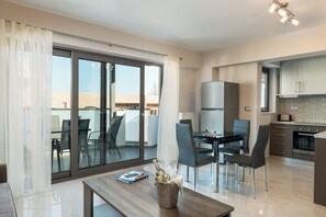 A modern kitchen with a refrigerator, oven, and a dining area with chairs and a table. - Jasmine Cozy & Modern Flat, steps from Sandy Beach (Maleme)