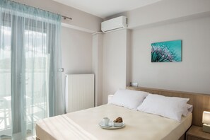 A neatly made bed with a cup and a bowl on a tray, a painting on the wall, and an air conditioner mounted above the bed. - Jasmine Cozy & Modern Flat, steps from Sandy Beach (Maleme)