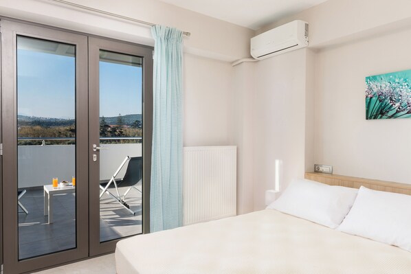A hotel room with a bed, a view of the outdoors, a radiator, and a painting on the wall. - Jasmine Cozy & Modern Flat, steps from Sandy Beach (Maleme)