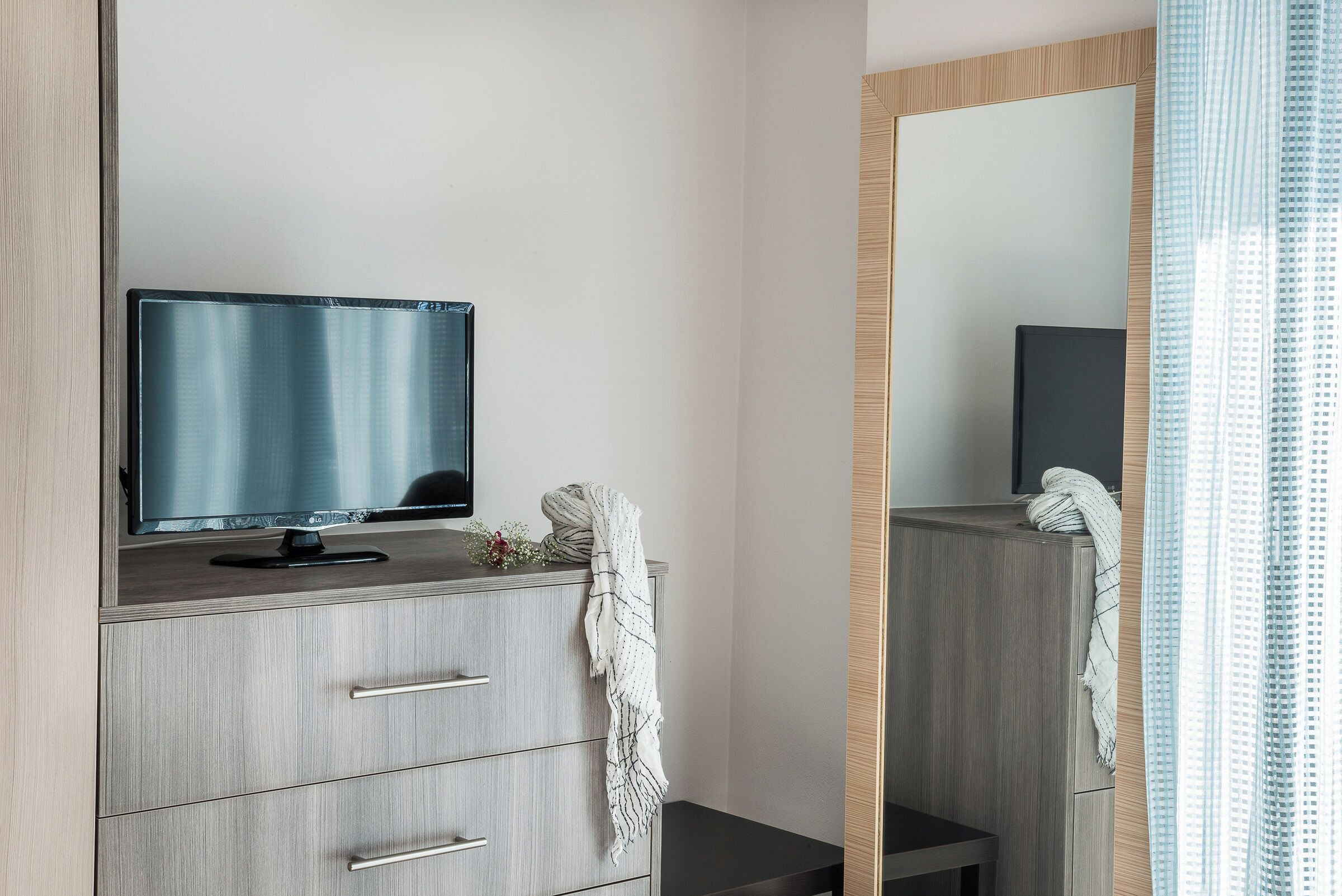 A modern bathroom with a wooden vanity, a flat-screen TV, and a mirror.