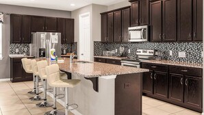 A modern kitchen with dark wood cabinets, a granite countertop, and a central island with bar stools. - Kissimmee Villa: 9BR Oasis, Sleeps 16 (Kissimmee)