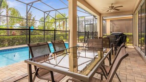 A glass-top dining table with chairs, a pool, and a patio area with a ceiling fan and grill. - Kissimmee Villa: 9BR Oasis, Sleeps 16 (Kissimmee)