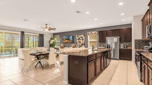 A modern kitchen with a central island, dark wood cabinets, and a large window overlooking a balcony. - Kissimmee Villa: 9BR Oasis, Sleeps 16 (Kissimmee)