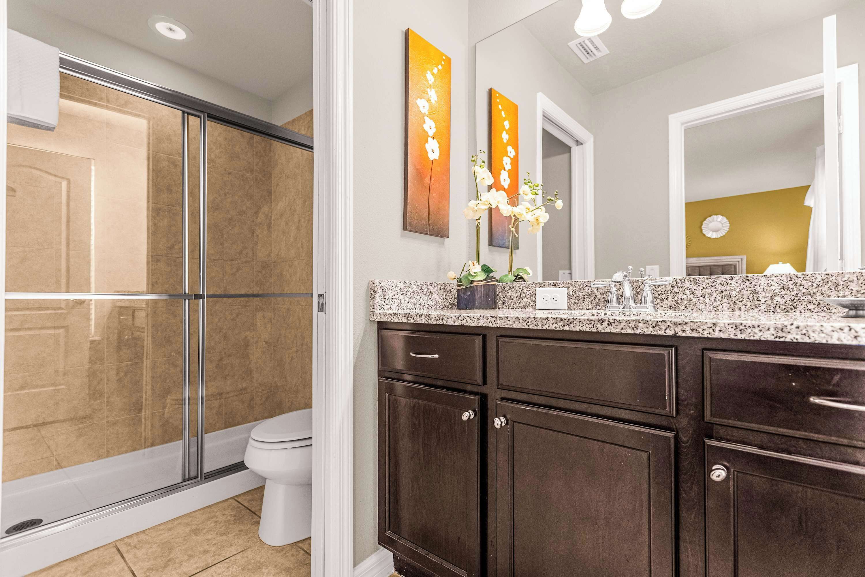 A bathroom with a glass shower enclosure, a toilet, dark wooden cabinets, and a granite countertop.