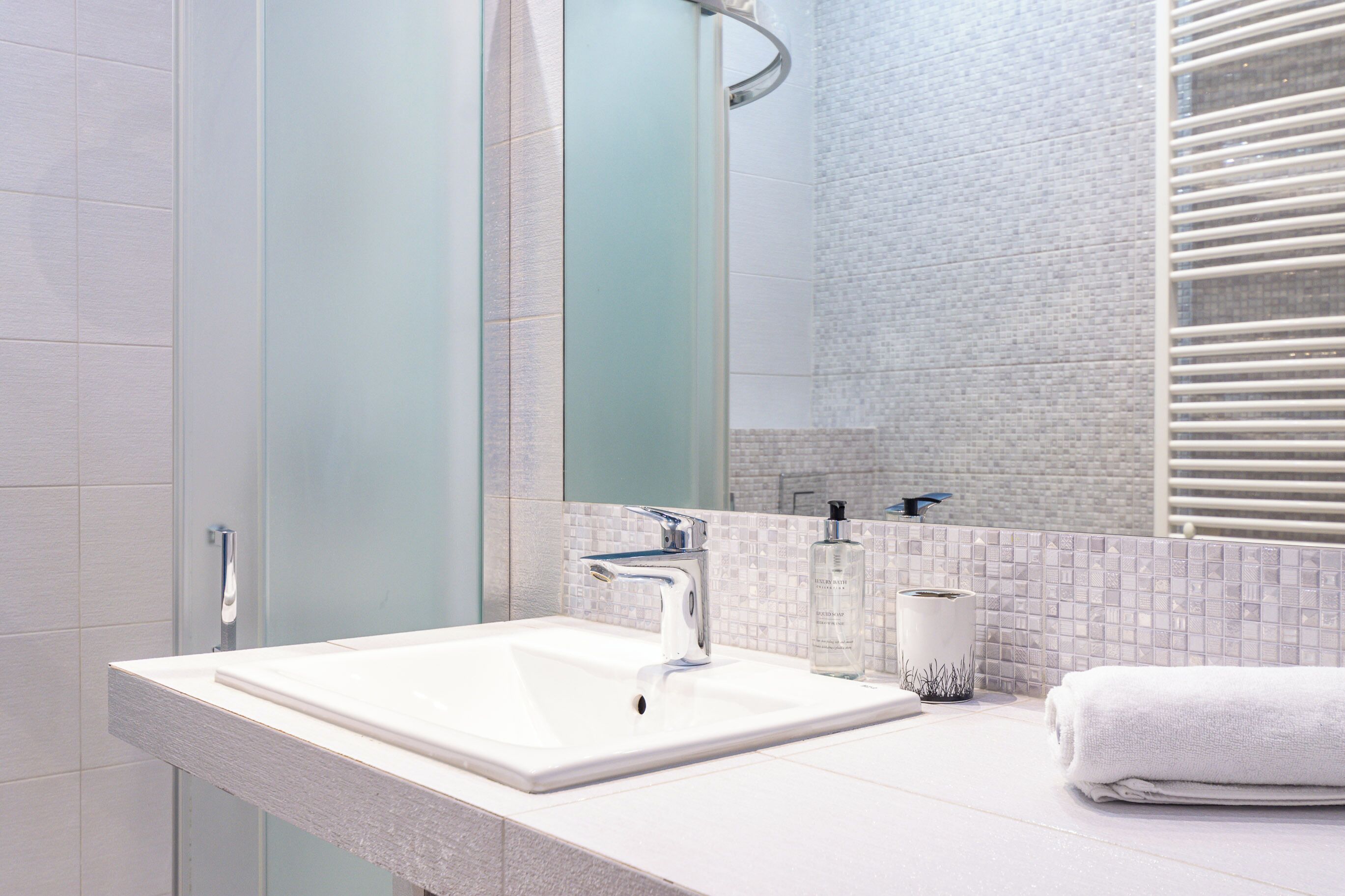 A modern bathroom with a large mirror, a white sink, and a towel.
