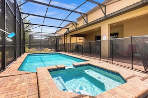 En swimmingpool med et glasindhegning, en terrasse med stole og et overdækket siddeområde.