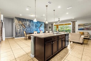 A spacious kitchen with a large island, modern pendant lighting, and a view to the outdoors. - Family-Friendly Villa: 9BR, Pool & Close to Disney (Kissimmee)