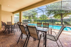 Eine Terrasse im Freien mit einem Glastisch und Stühlen, einem Swimmingpool und Blick auf Bäume und Gebäude.