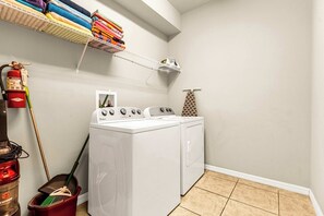 A laundry area with a washing machine, dryer, stacked laundry, a broom, and a fire extinguisher. - Family-Friendly Villa: 9BR, Pool & Close to Disney (Kissimmee)