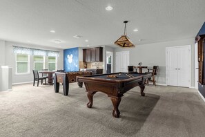Una habitación amplia con mesa de billar, comedor y cocina.