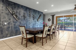 Un comedor con una mesa y sillas de madera oscura, una pared con textura y vista a una piscina.