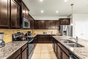 A kitchen with dark wood cabinets, a stainless steel refrigerator, a granite countertop, and a built-in oven. - Family-Friendly Villa: 9BR, Pool & Close to Disney (Kissimmee)