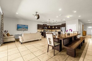 A spacious living area with a sofa, a dining table with benches, a kitchen with dark cabinets, and a ceiling fan.