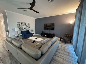 A modern living room with a sectional sofa, a coffee table, a TV, and a ceiling fan. - Modern 6BR Villa Kissimmee | Perfect for 14 Guests (Kissimmee)