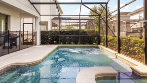 A swimming pool with a glass enclosure, surrounded by a white building and a hedge.