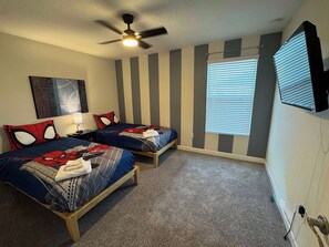 Une chambre avec deux lits, un ventilateur de plafond, une fenêtre avec des stores et un téléviseur fixé au mur.