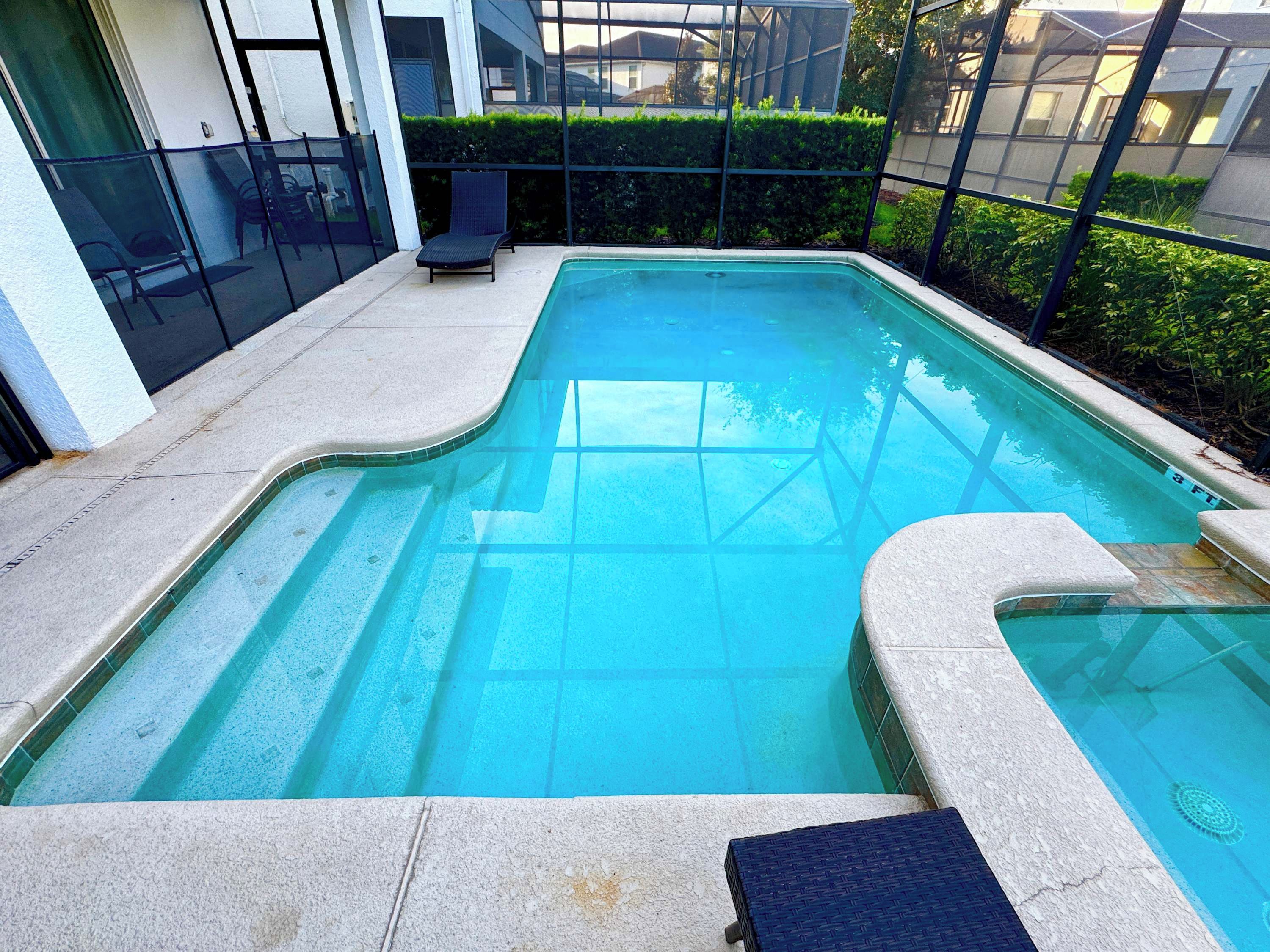 Una piscina rectangular amb un videt de rajola, envoltada per un sòl de formigó i una tanca metàl·lica.
