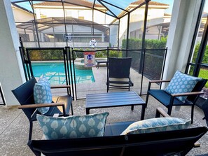 Un patio couvert avec des meubles d’extérieur, une piscine et un panneau indiquant la présence d’un sauveteur.
