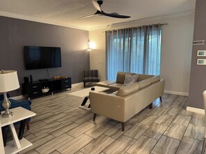 A modern living room with a flat-screen TV, a sofa, a coffee table, and a ceiling fan.