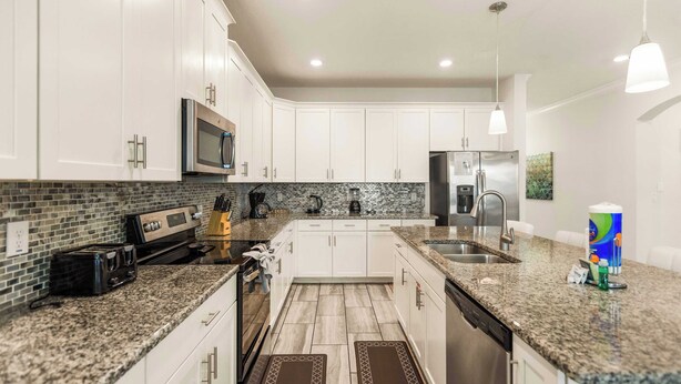 A modern kitchen with white cabinets, granite countertops, stainless steel appliances, and a tiled backsplash.