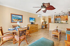 A dining area with a round table, chairs, and a ceiling fan. There is a kitchen area with a microwave and a sign that says "LET'S DO SUNSET". - Relax with lush lanai views and poolside access (Lahaina)