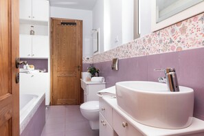 A bathroom with a white sink, a toilet, and a bathtub. There is a wooden door and a shelf with toiletries. - Astarte Villas - Stilvi 4 Bedroom Private Villa With Pool (RV3V+9Q3 Zakynthos, Greece)