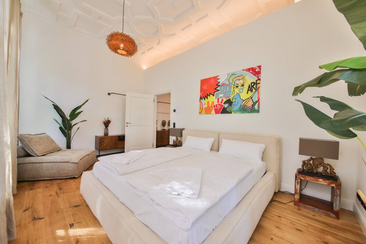 Ein Schlafzimmer mit einem großen Bett, einem Sofa, einer Pflanze und einem Bild an der Wand.