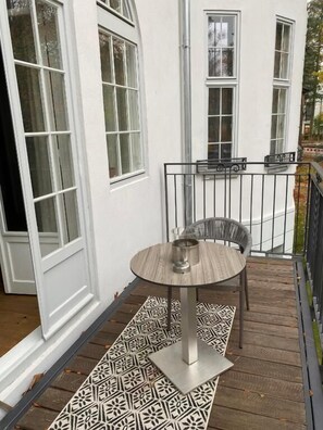 A wooden deck with a patterned rug, a round table with chairs, and a metal railing. - Aeronaut Suites powered by Pearl1 (Berlin)
