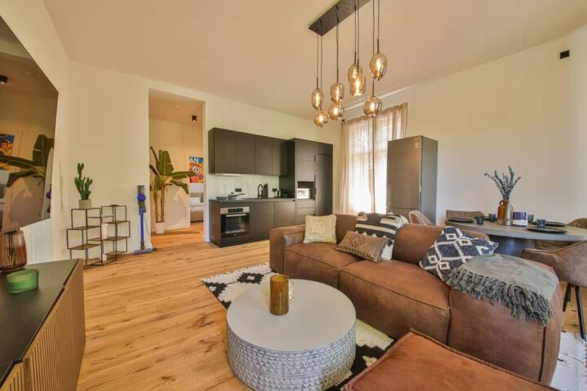 Ein modernes Wohnzimmer mit einer braunen Ledersofa, einem runden Couchtisch und einer Küche im Hintergrund.