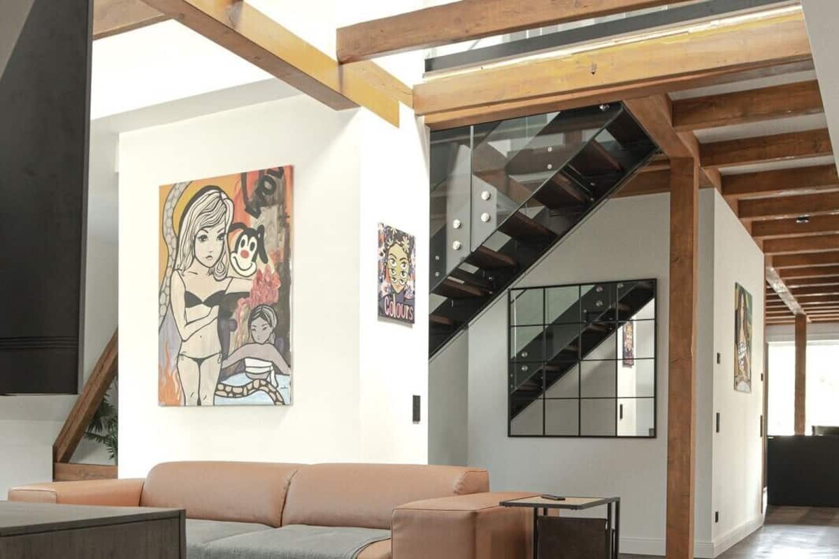 Ein geräumiges Loft mit hoher Decke, freiliegenden Holzbalken, einem großen Sofa, einem kleinen Tisch und Kunstwerken an den Wänden.