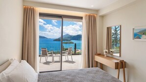 A hotel room with a bed, a desk, a chair, and a large sliding glass door leading to a balcony with a view of the sea and mountains. - Brand new Spacious 6 bedroom villa with stunning view, close to beach. (Lefkada)