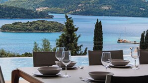 A dining table with chairs and empty plates, overlooking a body of water with boats and a distant island. - Brand new Spacious 6 bedroom villa with stunning view, close to beach. (Lefkada)