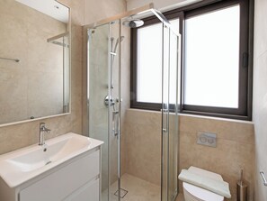 Moderni kylpyhuone, jossa on lasiseinällä varustettu suihku, valkoinen pesuallas ja wc.