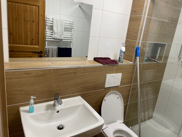 A bathroom with a wooden vanity, a sink, a mirror, a toilet, and a shower area. - Alpen-hostel Nordgrat 7 Buxacher Straße 23 mit Motorradvermietung (Memmingen)