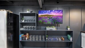 Un saló modern amb un televisor de pantalla plana gran muntat a la paret, un moble de fusta fosca amb prestatges que contenen diversos objectes de vidre i decoratius, i una petita planta en test.