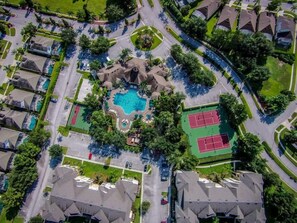 An aerial view of a residential area with a swimming pool, tennis courts, and a central landscaped area.