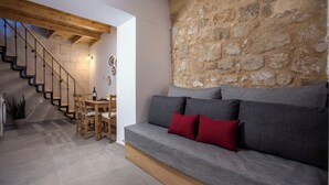 Un salon moderne avec un mur en pierre, un canapé gris agrémenté de coussins rouges, un escalier en bois et un coin repas.