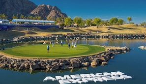 Ein Golfplatz mit einem Wasserspiegel, einem Berg im Hintergrund und einem großen Schild mit der Aufschrift 'AMERICAN EXPRESS'.